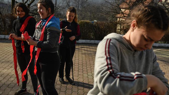 Gadis-gadis Rumania mengenakan sarung tinju sebelum latihan di Sarata Monteoru, sebuah kota kecil wisata di perbukitan Carpathians Timur di Rumania (14/1/2020). Saat ini Steluta Duta lebih banyak membantu generasi berikutnya untuk mengatasi rintangan di atas ring. (AFP/Daniel Mihailescu)