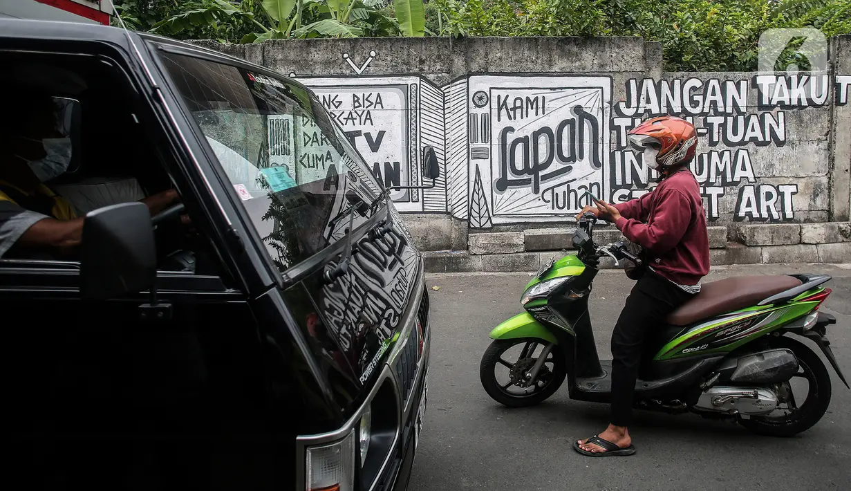 Pengendara melintas di depan mural bertuliskan “Kami Lapar Tuhan” di kawasan Jakarta Pusat, Selasa (24/8/2021). Mural 'Tuhan Aku Lapar' yang viral di jagat maya pada akhir Juli 2021 lalu, membuka rentetan peristiwa penghapusan mural di kota-kota besar Indonesia. (Liputan6.com/Johan Tallo)
