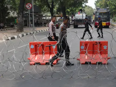 Personel Kepolisian melintas dibalik barikade kawat berduri yang menutup ruas Jalan Medan Merdeka Barat, Jakarta, Senin (28/10/2019). Penutupan ini antisipasi aksi unjuk rasa mahasiswa mendesak Presiden Jokowi segera mengeluarkan Perppu KPK. (Liputan6.com/Helmi Fithriansyah)