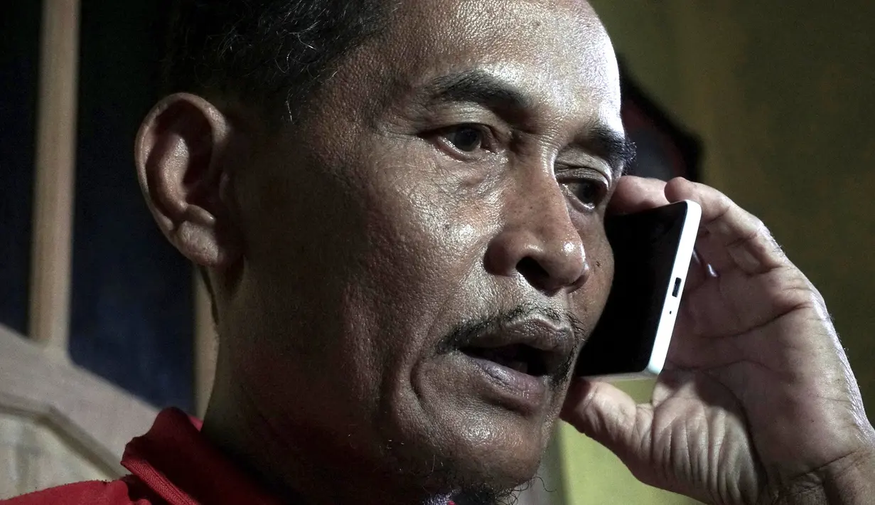 Bapak Sumarti Ningsih, Ahmad Kaliman berbincang lewat ponsel mengenai sidang pembunuhan anaknya di Cilacap, Jawa Tengah , Indonesia (8/11). Rurik Jutting telah dinyatakan dijatuhi hukuman penjara seumur hidup. (REUTERS/Idhad Zakaria)