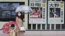 Warga Jepang mengenakan masker berjalan melewati poster yang berisi informasi peraih medali emas dari Jepang di Olimpiade Tokyo, Selasa (27/7/2021). (Foto: AP/Koji Sasahara)