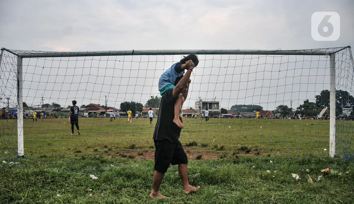 Warga menggendong anaknya menyaksikan 'Liga Kocok' di Desa Ragajaya, Bojong Gede, Kabupaten Bogor, Jawa Barat, Minggu (17/10/2021). Liga ini udah tradisi kita gelar tiap tahun. Siapa aja boleh ikut, yang penting warga Ragajaya." Jelas Rahmat, panitia turnamen.  (merdeka.com/Iqbal S. Nugroho)