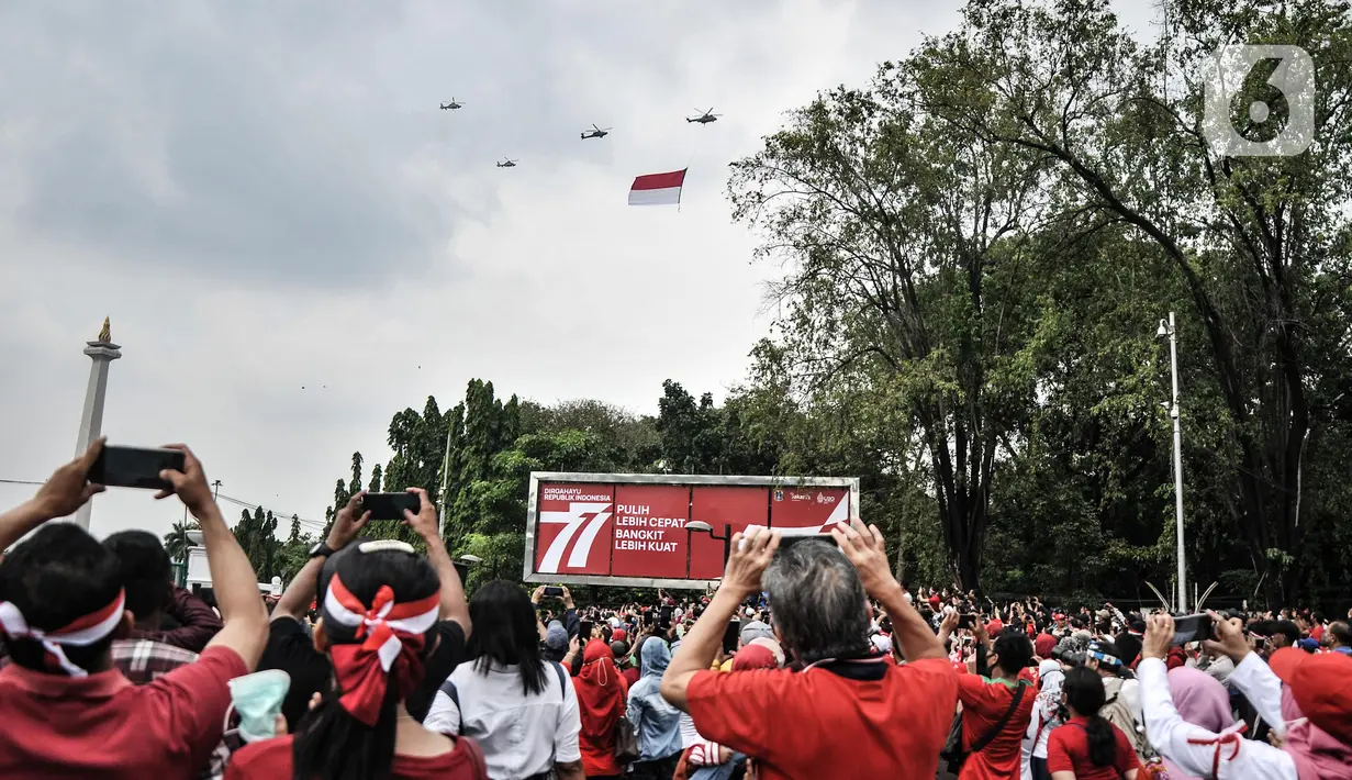 Warga menyaksikan manuver helikopter TNI AU membawa bendera Merah Putih saat perayaan HUT ke-77 Republik Indonesia (RI) di Taman Aspirasi Monumen Nasional (Monas), Jakarta Pusat, Rabu (17/8/2022).  Aksi akrobatik pesawat tempur dan helikopter yang membawa bendera Merah Putih tersebut disambut antusias oleh warga yang datang untuk mengikuti upacara Kemerdekaan RI. (merdeka.com/Iqbal S Nugroho)