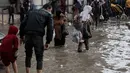 Ribuan warga pengungsi berjuang menahan masuknya air ke dalam tenda-tenda darurat di tengah kondisi kehidupan yang semakin berat menjelang musim dingin. Tampak dalam foto, orang-orang berjalan di tengah banjir di kamp darurat yang menampung warga Palestina yang terlantar setelah hujan deras di Kota Gaza pada Selasa 25 November 2025. (Omar AL-QATTAA/AFP)