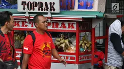 Dua pria berjalan melewati pedagang ketoprak yang menjajakan dagangannya di sisi jalan sekitar kawasan Patung Kuda Jakarta, Rabu (5/1/2019). Mereka mencoba peruntungan saat para buruh melakukan aksi perayaan Hari Buruh International atau May Day. (Liputan6.com/Helmi Fithriansyah)