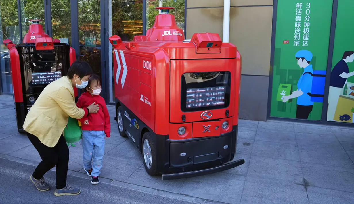 Wanita dan anak yang mengenakan masker melihat kendaraan pengiriman otonom dari JD.com di jalanan Beijing, China, Jumat (28/5/2021). Anak perusahaan China JD.com, JD Logistics, diberi izin untuk menjalankan kendaraan di jalan terbuka yang ditentukan di tenggara Beijing. (AP Photo/Ng Han Guan)