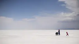 Penjual kerajinan berjalan bersama seorang gadis di Salar de Uyuni, dataran garam terbesar di dunia, di Uyuni, Bolivia, pada 7 November 2020. Dikenal sebagai dataran garam terluas di dunia karena Salar de Uyuni memiliki luas sekitar 4.086 kilometer persegi. (RONALDO SCHEMIDT/AFP)