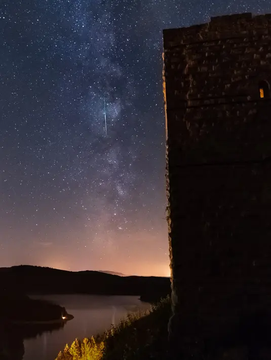 Sebuah meteor melintasi langit malam melalui Bima Sakti selama hujan meteor tahunan Perseid di danau Pierre-Percee, Perancis timur, Minggu (12/8). Puncak hujan meteor terjadi pada 11-12 Agustus dan 12-13 Agustus. (Patrick HERTZOG / AFP)