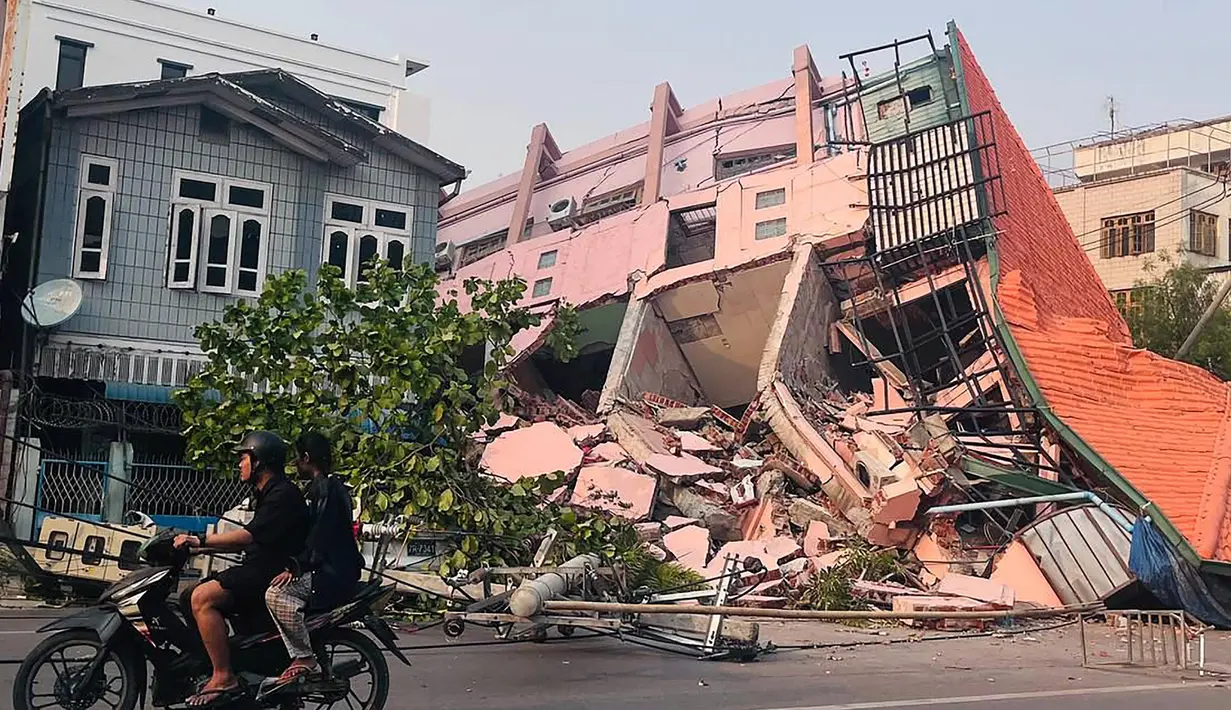 Orang-orang mengendarai sepeda motor melewati sebuah bangunan yang runtuh di Mandalay pada tanggal 28 Maret 2025, setelah gempa bumi di Myanmar tengah. (Foto: AFP)