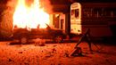 Pengunjuk rasa melemparkan benda ke bus di sebelah mobil polisi yang terbakar selama demonstrasi di luar rumah presiden Sri Lanka di Kolombo (31/3/2022). Tidak dijualnya Diesel melumpuhkan transportasi yang terkena dampak mengalami pemadaman listrik yang sangat lama. (AFP/Ishara S. Kodikara)