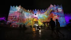 Orang-orang berjalan di dekat gerbang Damaskus selama festival cahaya di kota tua Yerusalem, 28 Juni 2018. Festival cahaya yang menampilkan karya seniman Israel dan internasional ini berlangsung setiap tahun di Kota Tua Yerusalem. (AFP / Ahmad GHARABLI)
