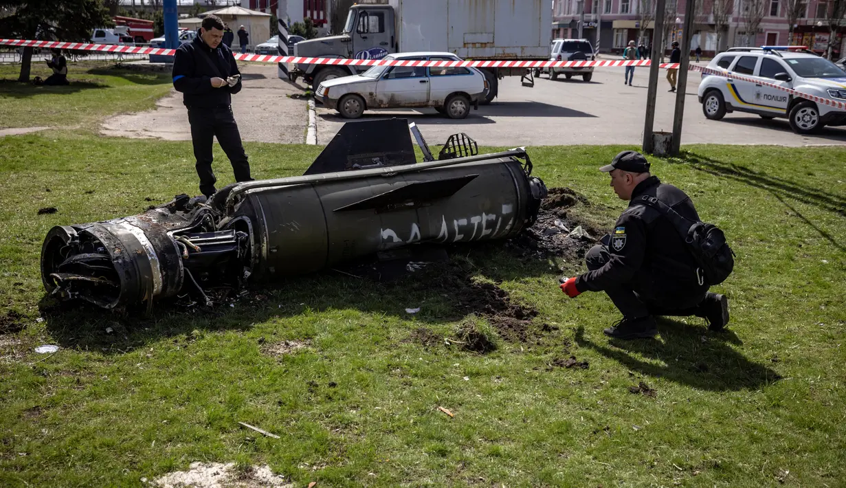 Polisi Ukraina memeriksa sisa-sisa roket besar dengan tulisan "untuk anak-anak kita" dalam bahasa Rusia di sebelah bangunan utama stasiun kereta api yang digunakan untuk evakuasi warga sipil, yang terkena serangan roket di Kramatorsk, Ukraina timur (8/4/2022). (AFP/Fadel Senna)