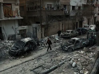 Seorang pria berjalan di antara bangunan yang hancur akibat  serangan udara dari rezim pemerintah Suriah di Ghouta Timur, Minggu (25/2). Wilayah yang dikuasai pemberontak tersebut terus dibombardir selama lima hari terakhir. (HAMZA AL-AJWEH/AFP)