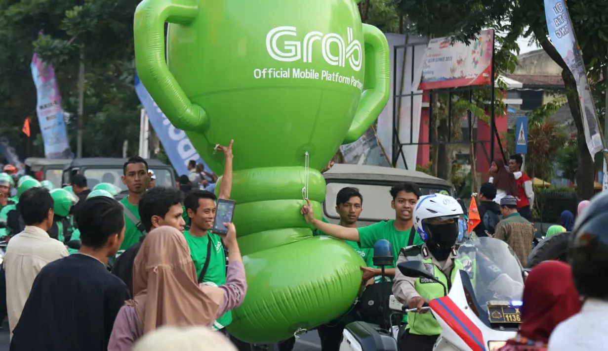 Mitra dari Grab membawa balon raksasa saat obor Asian Games XVIII melintas di Kota Malang, Jawa Timur, Jumat (20/7/2018). Sebanyak 53 kota di Indonesia akan dilalui oleh obor Asian Games. (Bola.com/Aditya Wani)