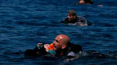 Seorang pengungsi Suriah menggendong bayi sambil berenang menuju pantai setelah perahu yang mereka naiki kempes sebelum mencapai pulau Yunani Lesbos, 12 September 2015. (REUTERS/Alkis Konstantinidis)  