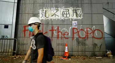 Seorang demonstran berjalan melewati markas polisi yang ditulisi 'Never Give In', Hong Kong, Jumat (21/6/2019). Markas polisi tersebut jadi korban aksi vandalime demonstran dalam lanjutan aksi unjuk rasa menolak RUU Ekstradisi. (AP Photo/Vincent Yu)