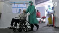 Petugas medis mendorong pasien yang duduk di kursi roda di depan UGD RSUD Cengkareng, Jakarta, Kamis (24/6/2021). Lonjakan kasus virus corona mengakibatkan ruang IGD penuh, pihak rumah sakit lantas mendirikan tenda darurat untuk merawat pasien covid-19. (merdeka.com/Arie Basuki)