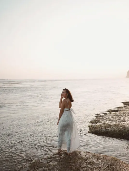 Nikmati senja di pinggir pantai memang selalu menjadi momen yang dinantikan oleh semua orang ketika berkunjung ke pantai, tak terkecuali Pamela Bowie. Selain nikmati air laut dengan pasir pantai, nikmati air laut dengan berdiri di atas batu besar pinggir pantai memang jadi spot menarik. (Liputan6.com/IG/@pammybowie)