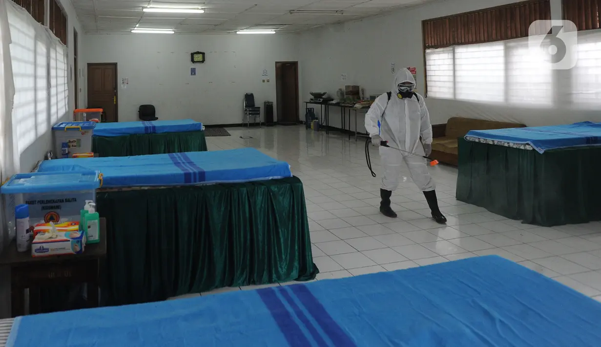 Petugas gugus tugas Covid-19 RW 03 menyemprotkan desinfektan pada tempat tidur untuk isolasi mandiri di Gedung Sasana Krida Karang Taruna, Kelurahan Pondok Labu, Jakarta, Selasa (19/1/2020). Gedung itu disulap oleh warga setempat untuk dijadikan tempat isolasi mandiri. (merdeka.com/Arie Basuki)