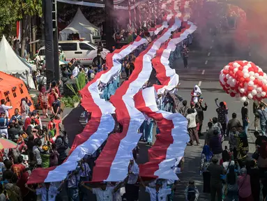 Para siswa dari berbagai sekolah membentangkan bendera Merah Putih panjang saat berbaris di jalan-jalan selama acara upacara untuk memperingati HUT ke-80 Kemerdekaan Indonesia di Surabaya, Jawa Timur pada 17 Agustus 2025. (Juni KRISWANTO/AFP)