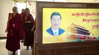 Para biksu berjalan melewati poster dengan potret Presiden China Xi Jinping dan Gerbang Tiananmen di Tibetan Buddhist College dekat Lhasa di Daerah Otonomi Tibet China barat, Senin, 31 Mei 2021 (AP)