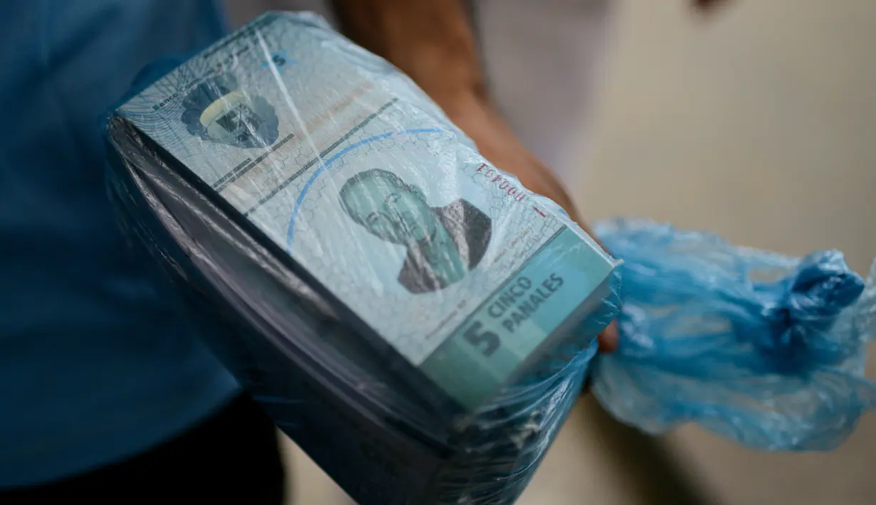 Seorang pria membawa setumpuk uang lokal baru di Caracas, Venezuela (15/12). Sebuah kota kumuh di puncak bukit di Caracas menciptakan mata uangnya sendiri yang bernama Panal. (AFP Photo/Federico Parra)