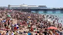 Kerumunan pengunjung berkumpul di pantai untuk menikmati hari terpanas tahun ini di Brighton, Inggris, Kamis (25/6/2020). Pantai tersebut diserbu warga Inggris, setelah masa pelonggaran pembatasan sosial akibat covid-19 dan pembatasan perjalanan Eropa. (Gareth Fuller/PA via AP)