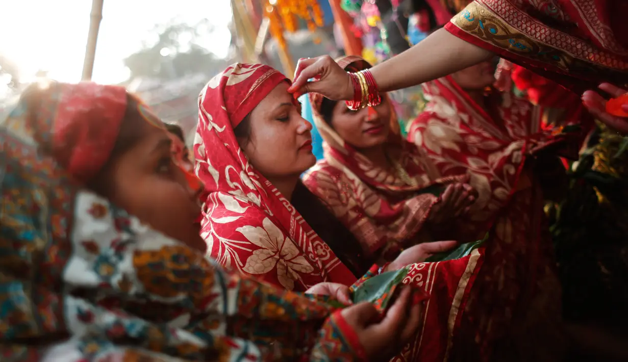 Seorang wanita Nepal mengenakan bubuk vermilion di dahi wanita lain di tepi Sungai Bagmati selama festival Chhath Puja di Kathmandu, Nepal (26/10). Para wanita ini melakukan doa saat matahari terbenam. (AP Photo/Niranjan Shrestha)
