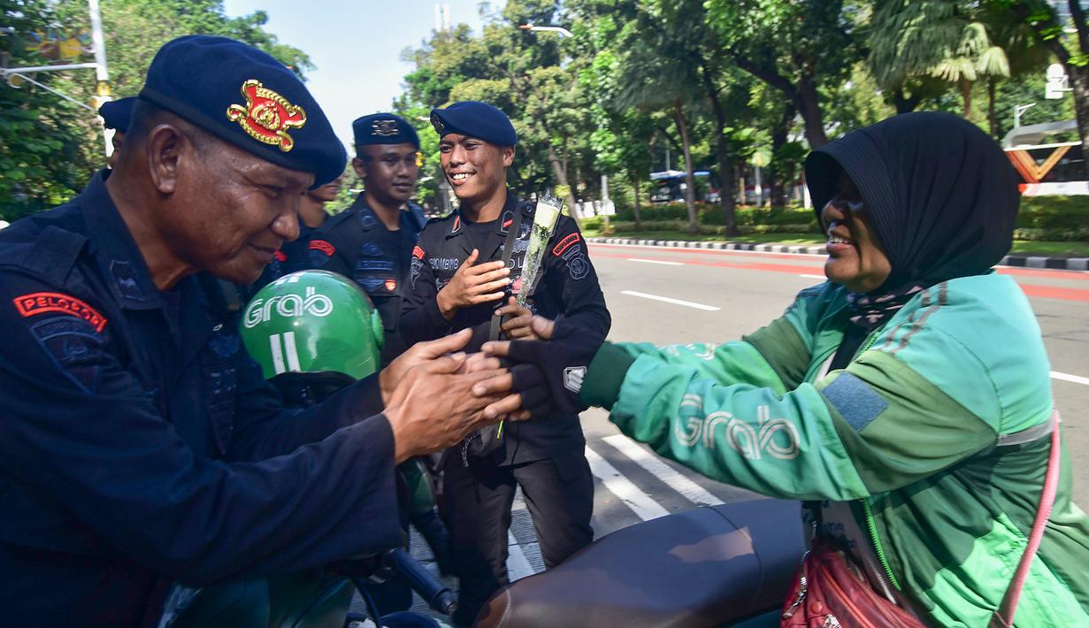 Pengemudi ojek daring/online (ojol) memberikan bunga mawar kepada salah satu personel kepolisian dari unsur Korps Brigade Mobil (Brimob) di sekitar kawasan Monumen Nasional, Jakarta, Selasa (2/9/2025). (merdeka.com/Arie Basuki)