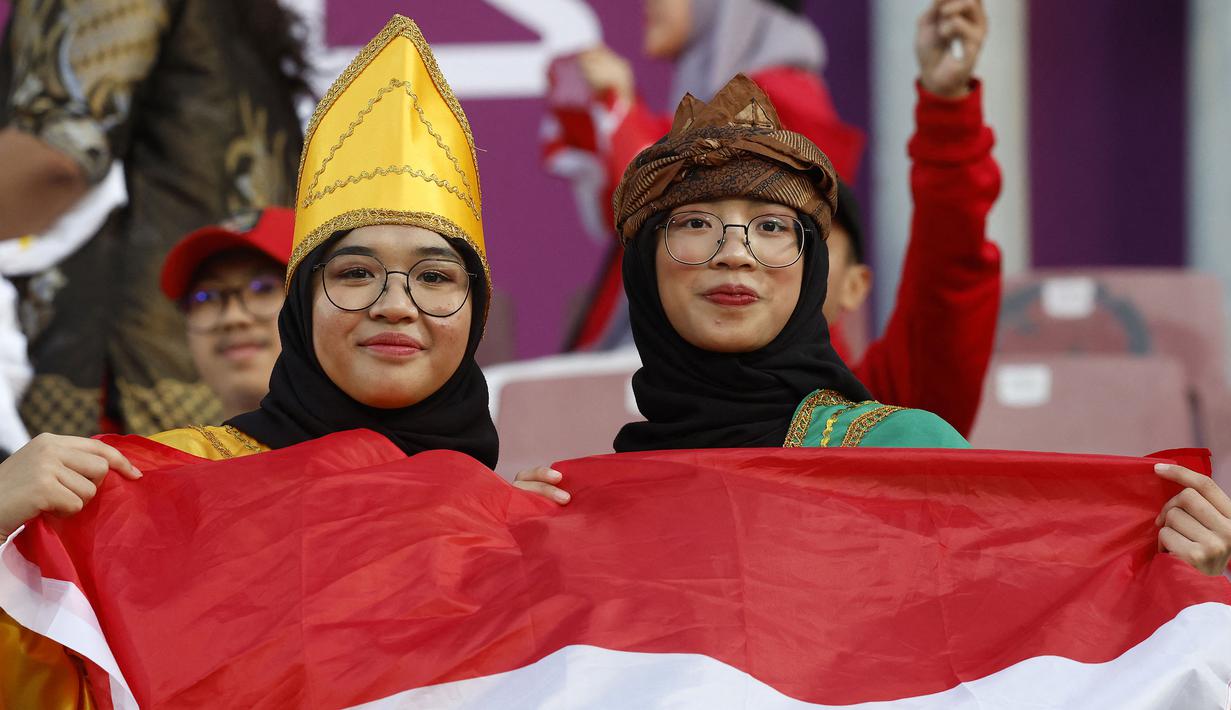 Dua suporter wanita Indonesia membentangkan bendera Merah Putih di tribun stadion sebelum dimulainya laga kedua Grup D Piala Asia 2023 antara Timnas Indonesia menghadapi Vietnam di Abdullah Bin Khalifa Stadium, Doha, Qatar, Jumat (19/1/2024). (AFP/Karim Jaafar)