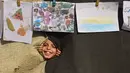 Seorang anak melihat melalui lubang di selimut selama pameran yang menampilkan koleksi gambar oleh anak-anak dan perempuan di sebuah sekolah yang diubah menjadi tempat penampungan bagi pengungsi Palestina di kawasan Al-Rimal, Kota Gaza, pada 5 November 2025. (Omar AL-QATTAA/AFP)