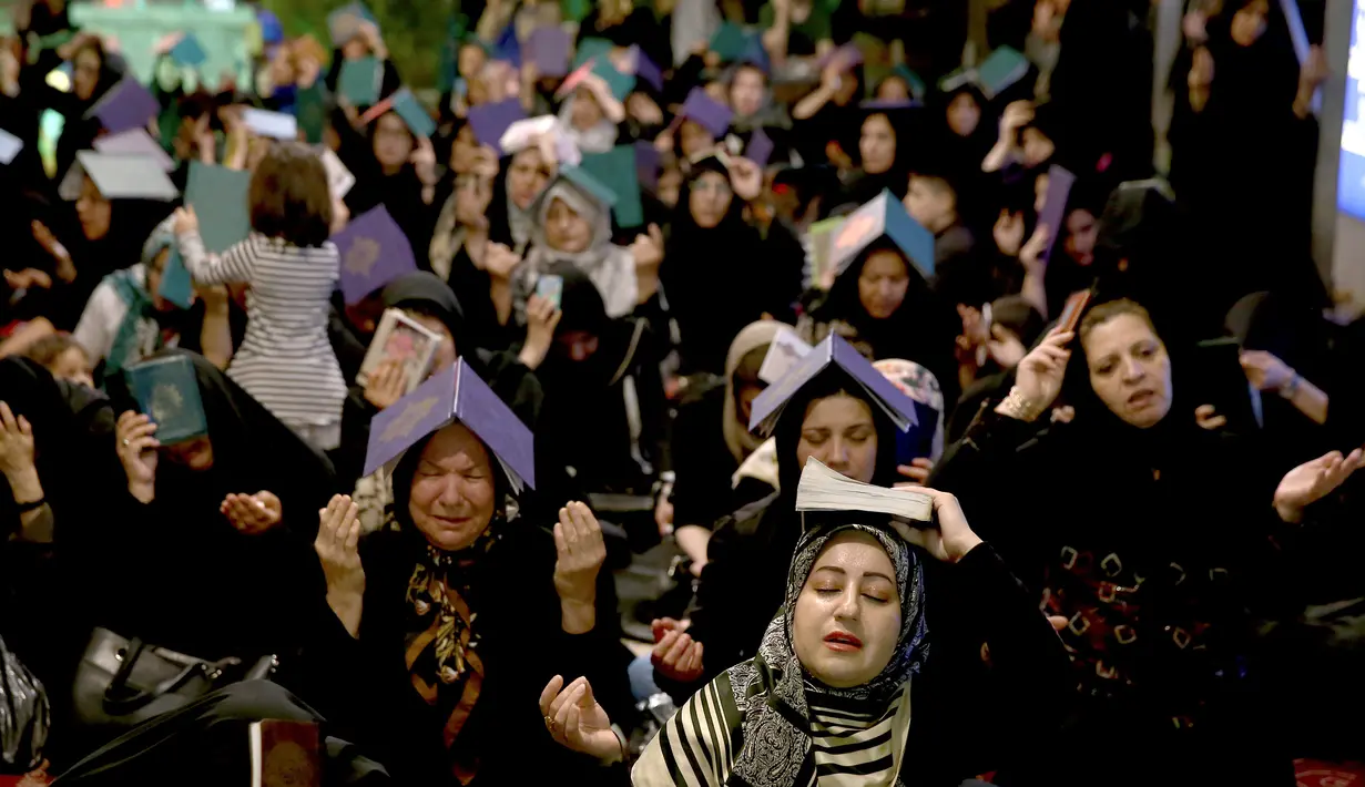Muslim Syiah Iran meletakkan mushaf Alquran di kepala mereka saat berburu malam Lailatul Qadar di Teheran, Iran, Jumat (8/6). Malam Lailatul Qadar  dipercaya sebagai malam pertama kali Alquran diturunkan kepada Nabi Muhammad. (AP Photo/Ebrahim Noroozi)
