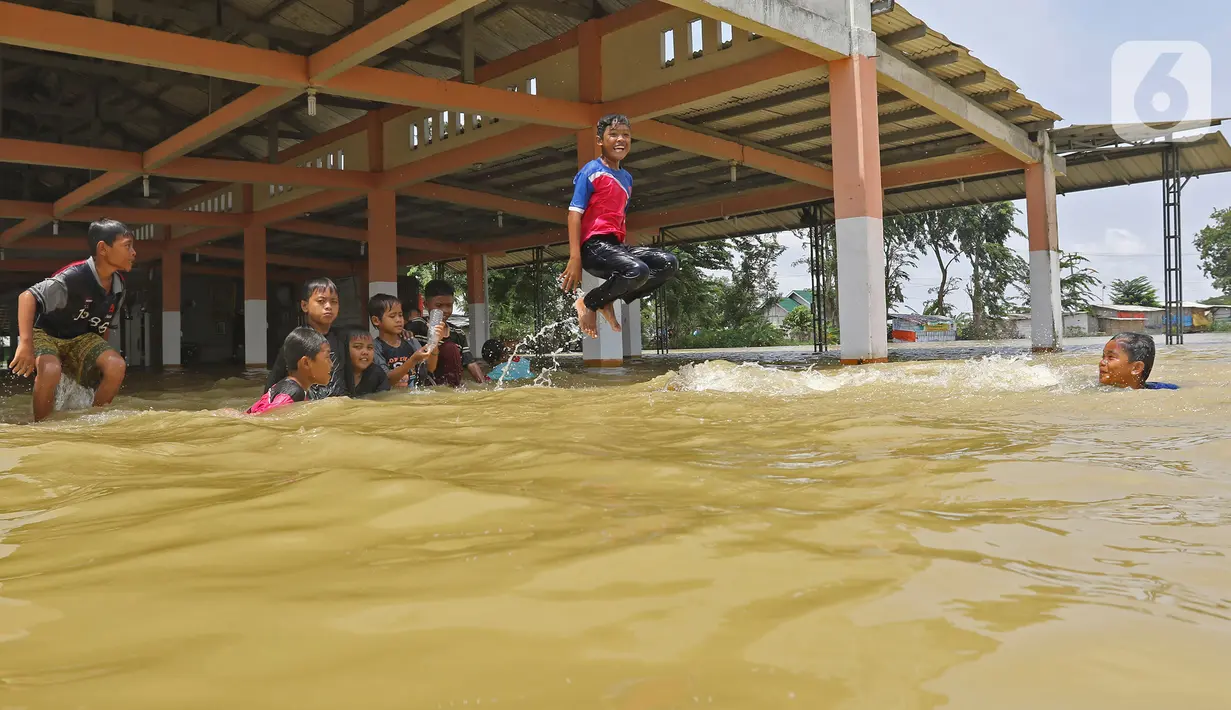 Anak-anak bermain banjir di Desa Sukalaksana Kabupaten Bekasi, Jawa Barat, Senin (22/02/2021). Jebolnya tanggul Sungai Citarum ini disebabkan oleh debit air yang tinggi. (Liputan6.com/Herman Zakharia)
