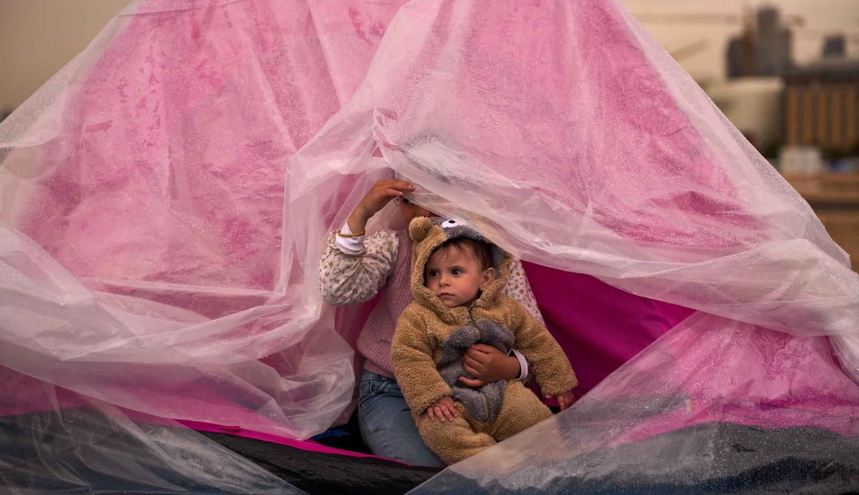 Yasmin menggendong saudara laki-lakinya, Ali, keduanya mengungsi dari pinggiran selatan Beirut, Dahiyeh, mereka berlindung dari hujan di dalam tenda di sepanjang pantai, Beirut, Lebanon, Kamis, 26 Maret 2026. Kondisi pengungsi di Lebanon saat ini berada dalam fase krisis kemanusiaan. (AP Photo/Emilio Morenatti)