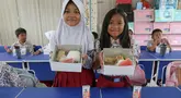 Dua siswi Sekolah Dasar (SD) Angkasa 5 Halim Perdanakusuma memperlihatkan makanan yang tersaji di dalam kotak saat uji coba program makan bergizi gratis, Jakarta, Selasa (26/11/2024). (Liputan6.com/Herman Zakharia)