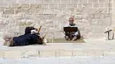 Seorang pria membaca ayat-ayat Alquran sementara pria lain beristirahat dekatnya saat mereka menunggu waktu berbuka puasa selama bulan suci Ramadhan di Masjid Al-Omari, Kota Gaza, Palestina, 13 April 2022. (AP Photo/Adel Hana)