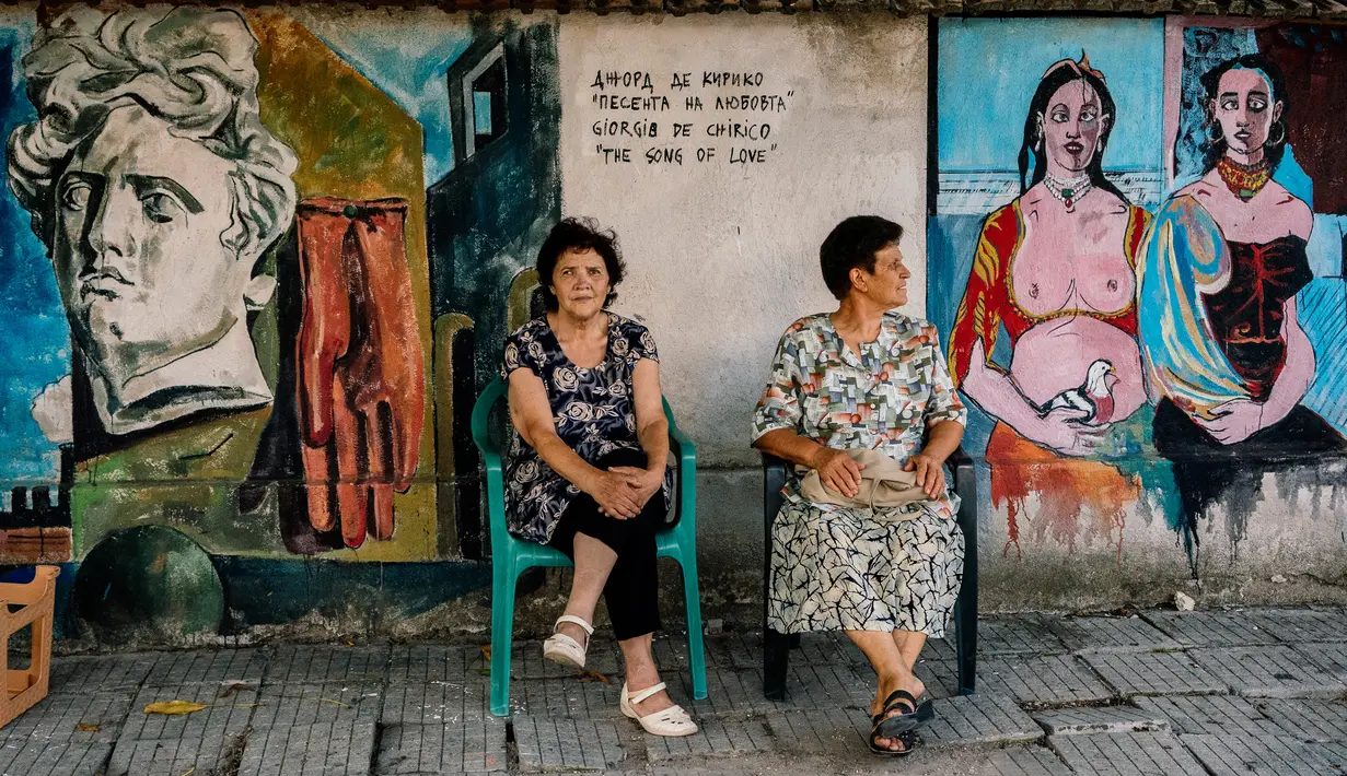 Warga duduk di depan lukisan mural seniman terkenal di  dinding desa Staro Zhelezare, Bulgaria, 4 Agustus 2018. Mural bagian dari proyek tahunan itu diluncurkan oleh wanita Polandia, Katarzyna Piriankov dan suaminya, Ventzislav. (AFP/Dimitar DILKOFF)