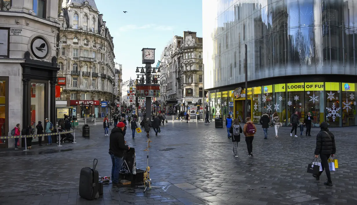 Pembeli berjalan kaki membawa tas belanjaan di Leicester Square setelah pelonggaran pembatasan virus corona COVID-19 menyusul berakhirnya kebijakan penguncian nasional atau lockdown kedua di Inggris, di London, Sabtu (5/12/2020). (AP Photo/Alberto Pezzali)
