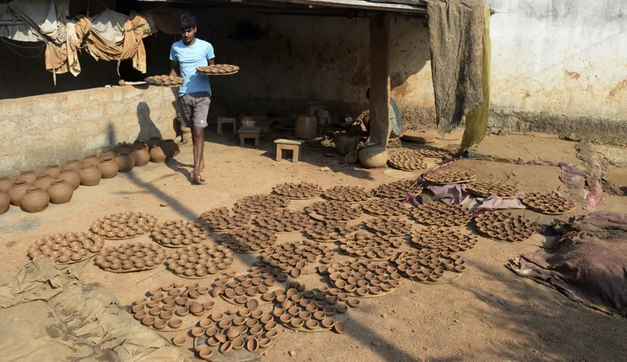Seorang perajin tembikar membawa diyas atau pot minyak untuk dikeringkan di pinggiran Hyderabad, India, 26 Oktober 2021. Diwali adalah salah satu festival besar yang dirayakan oleh umat Hindu, Jain, Sikh dan beberapa umat Buddha, terutama umat Buddha Newar. (NOAH SEELAM/AFP)