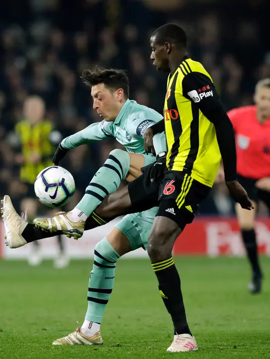 Gelandang Arsenal, Mesut Ozil berebut bola dengan pemain Watford, Abdoulaye Doucoure dalam laga lanjutan Premier League 2018-19 pekan ke-34 di Vicarage Road, Senin (15/4). Arsenal sukses mengalahkan tuan rumah Watford dengan skor tipis 1-0. (AP Photo/Matt Dunham)