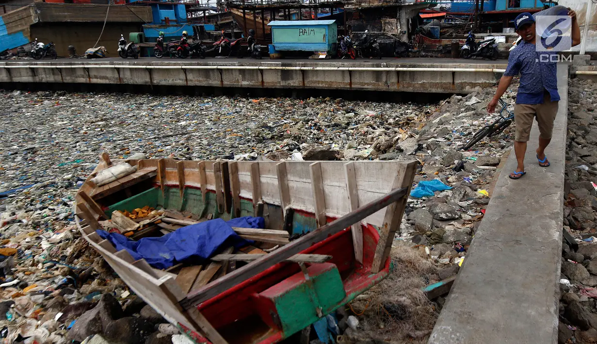 Warga melintas dekat tumpukan sampah yang menutupi di pinggir laut kawasan Pelabuhan Muara Baru, Jakarta Utara, Senin (29/7/2019). Sampah-sampah yang didominasi oleh sampah plastik ini terbawa arus laut yang dibuang masyarakat secara sembarangan. (Liputan6.com/Johan Tallo)