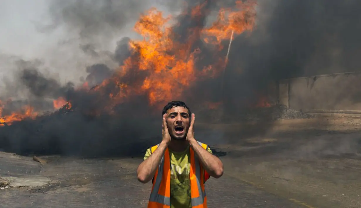 Petugas pemadam kebakaran Palestina berteriak saat berusaha memadamkan api yang berkobar di salah satu gudang di barat kota Gaza, (12/7/2014). (AFP PHOTO/Mahmud Hams)
