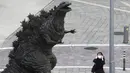 Seorang wanita menyesuaikan masker wajahnya saat berjalan dekat patung Godzilla di Tokyo, Jepang, Jumat (16/10/2020). Ibu Kota Jepang itu mengonfirmasi lebih dari 180 kasus virus corona COVID-19 baru pada hari Jumat. (AP Photo/Hiro Komae)