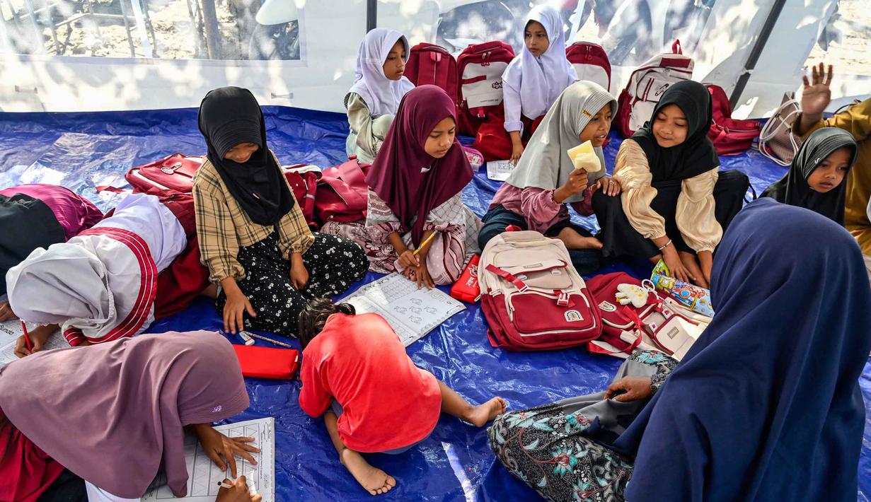 Belum terlihat tanda-tanda pembersihan lumpur baik di luar maupun di dalam ruangan belajar. Tampak dalam foto, para siswa berkumpul di kelas darurat di dalam tempat penampungan setelah sekolah mereka hancur akibat banjir bandang di daerah yang berdekatan dengan Sungai Peusangan di Bireuen, provinsi Aceh, Senin 5 Januari 2026. (CHAIDEER MAHYUDDIN/AFP)
