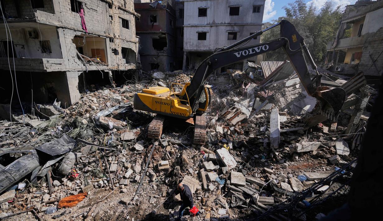 Data Kementerian Kesehatan Lebanon, per 4 April 2026, mencatat 1.368 warga sipil tewas dan 4.138 luka-luka akibat serangan udara Israel. Tampak dalam foto, sebuah ekskavator membersihkan puing-puing sementara seorang pria membawa barang-barang miliknya berjalan melewati reruntuhan di lokasi serangan Israel pada Minggu 5 April 2026 terhadap sebuah bangunan di lingkungan Jnah, Beirut, Lebanon, Senin 6 April 2026. (AP Photo/Hassan Ammar)