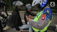 Petugas kepolisian lalu lintas saat menilang pengendara motor saat Operasi Zebra Jaya 2020 di kawasan Cawang, Jakarta, Senin (26/10/2020). Operasi Zebra Jaya dilaksanakan pada 26 Oktober-8 November 2020 untuk menekan jumlah pelanggaran lalu lintas. (Liputan6.com/Faizal Fanani)