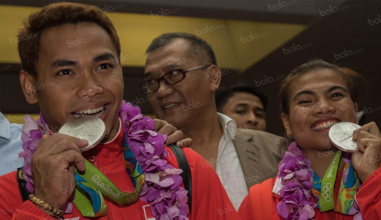 Lifter Indonesia, Eko Yuli dan Sri Wahyuni menggigit medali perak yang didapatnya saat Olimpiade 2016 Rio de Janeiro ketika kembali ke Indonesia. (Bola.com/Vitalis Yogi Trisna)