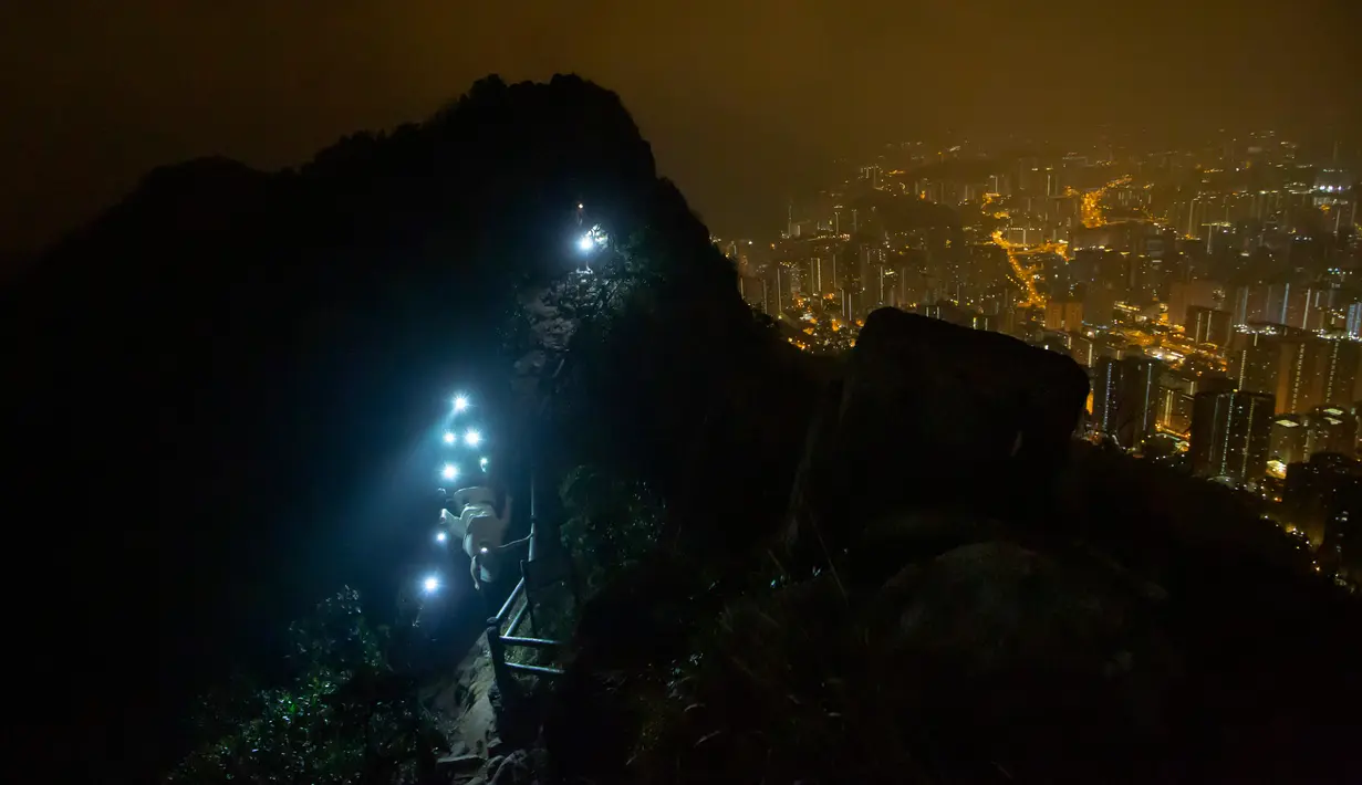 Demonstran antipemerintah membawa patung The Lady Liberty of Hong Kong untuk didirikan di puncak pegunungan Lion Rock, Hong Kong, Minggu (13/10/2019). Beberapa di antara demonstran mengenakan lampu kepala meski badai petir melanda semalaman. (AP Photo/Kin Cheung)