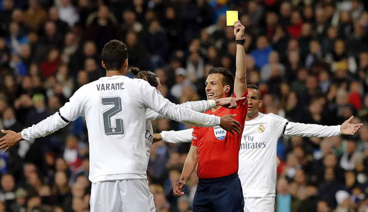 Wasit Estrada Fernandez memberikan kartu kuning kepada bek Real Madrid, Raphael Varane, pada laga La Liga Spanyol melawan Sevilla di Stadion Santiago Bernabeu, Madrid, Minggu (20/3/2016). Madrid menang 4-0 atas Sevilla. (EPA/Ballesteros)
