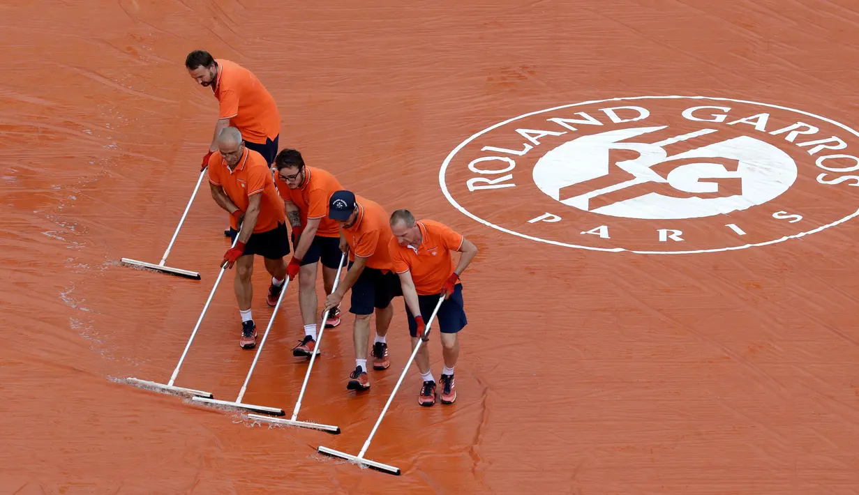 Pekerja stadion mengepel untuk membuang air hujan saat pertandingan perempat final Perancis Terbuka di stadion Roland Garros, Paris (6/6). (AP/Alessandra Tarantino)